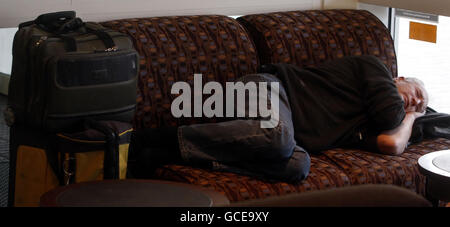 Un homme dort sur quelques chaises à l'aéroport de Glasgow alors que le chaos provoqué par une éruption volcanique en Islande continue. Banque D'Images