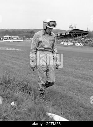 John Surtees, ancien motard champion du monde et maintenant coureur automobile, s'éloigne sans aucune blessure après un accident dans la coupe de la lavande lors de la rencontre de course automobile internationale à Goodwood. Banque D'Images