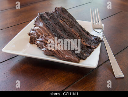 Grand morceau de gâteau au chocolat sur plaque blanche avec la fourchette sur la table en bois Banque D'Images