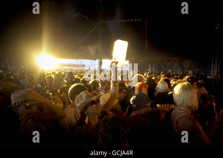 Un fêtard dans la foule tient une bouteille illuminée par le soleil couchant alors que les festivaliers de la tente WOW dans le village de danse attendent que Boy George se présente sur scène au festival Glastonbury à la ferme de Carry, Somerset. Banque D'Images