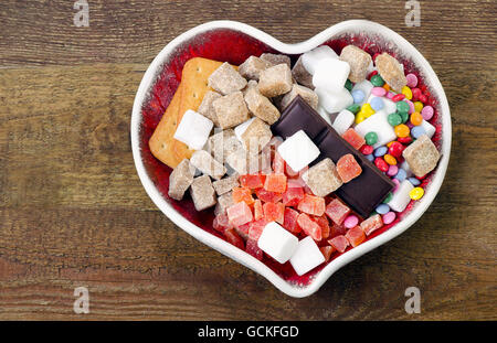 Différents types de sucre, bonbons et biscuits dans un bol en forme de coeur. Une mauvaise nutrition concept. Vue d'en haut Banque D'Images