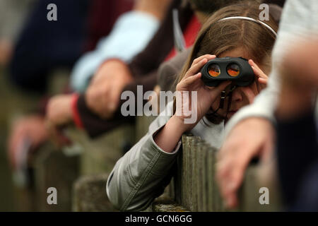 Un jeune spectateur regarde l'action à travers des jumelles sur le Cours de juillet à l'hippodrome de Newmarket Banque D'Images