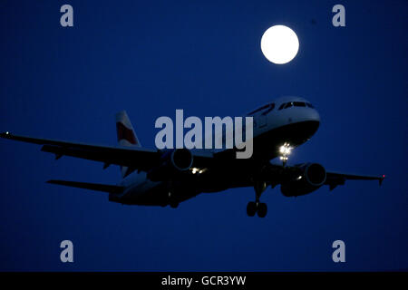 Une pleine lune brille dans le ciel lorsqu'un avion arrive à l'aéroport de Heathrow, Londres. Banque D'Images