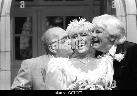 La barmaid de la rue du couronnement Bet Lynch (actrice Julie Goodyear) reçoit un baiser du marié de télévision Alec Gilroy (acteur Roy Barraclough), et le meilleur homme Charles Halliday (acteur Tony Booth), après le mariage à la télévision à l'église de la Sainte Trinité à Bolton, lancashire. Banque D'Images