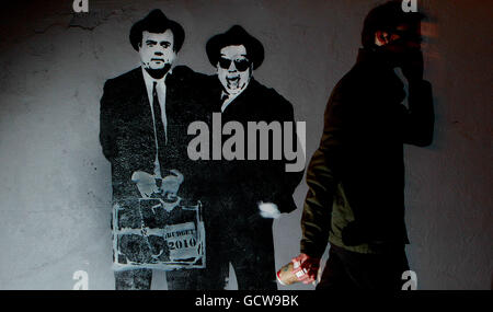 Un piéton rentre ce soir à la maison devant les graffitis de l'artiste ADW, représentant le ministre des Finances Brian Lenihan et Taoiseach Brian Cowen tandis que les Blues Brothers s'empaissent d'une mallette à budget dans le centre de Dublin. Banque D'Images