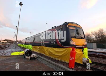 Le personnel de ScotRail ajuste la plinthe tandis que les soufflantes à gaz aident à dégivrer le train de roulement des trains, tandis que le nouveau ministre écossais des Transports Keith Brown utilise un spray de dégivrage « Kill Frost » qui empêche et facilite l'élimination de la glace du train de roulement d'un train lors d'une visite au dépôt Eastfield de ScotRail à Glasgow. Banque D'Images