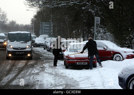 Un homme utilise un balai pour balayer la neige d'un des nombreux véhicules abandonnés sont laissés sur Reigate Hill près de Reigate, Surrey, alors que de grandes régions de la Grande-Bretagne ont été mis à l'arrêt aujourd'hui que le grand gel a resserré son emprise sur la nation. Banque D'Images