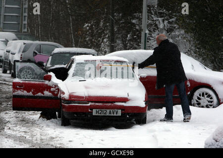 Un homme utilise un balai pour balayer la neige du pare-brise d'un des nombreux véhicules abandonnés sont laissés sur Reigate Hill près de Reigate, Surrey, alors que de grandes régions de la Grande-Bretagne ont été mis à l'arrêt aujourd'hui que le grand gel a resserré son adhérence sur la nation. Banque D'Images