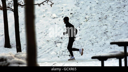 Un jogging dans la neige à Kelvingrove Park, Glasgow, alors que le gros gel se poursuit dans tout le Royaume-Uni. Banque D'Images