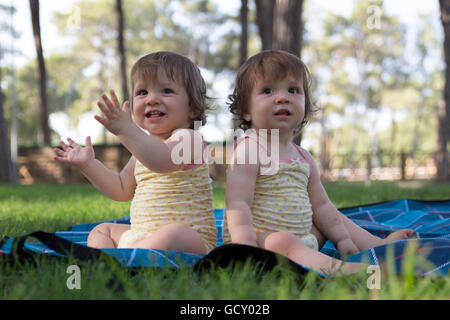 Heureux bébé twin sisters assis sur une couverture dans le parc Banque D'Images