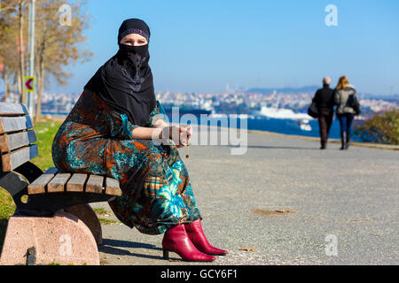 Style musulman habillé Femme assise sur banc en bois Banque D'Images