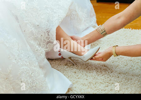 Préparation de mariage. Les amies de l'épouse de l'aider dans mes chaussures chaussures de mariage Banque D'Images