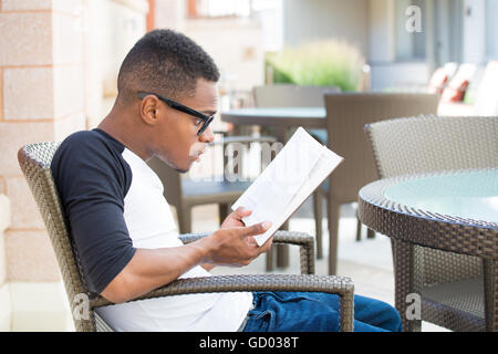 Libre shot, ordinateur geek jeune homme avec lunettes noires assis dans une chaise, choqué avec drôle de visage par parcelle histoire qu'il lit, Banque D'Images