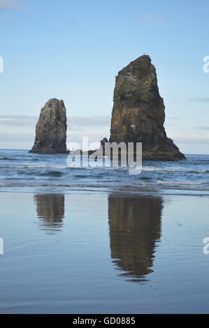 Les aiguilles à Cannon Beach, Oregon reflète dans l'eau et de sable humide. Banque D'Images