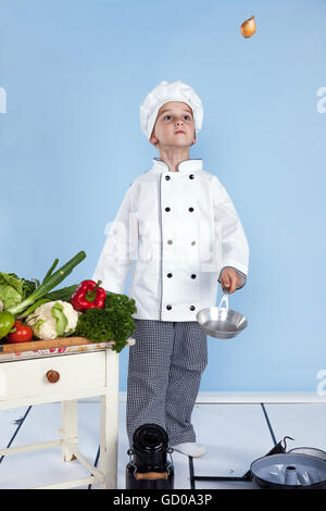 Jonglant avec les oignons dans une casserole - un petit garçon comme chef de cuisine en salade, avec des légumes. Isolé sur blanc. Banque D'Images