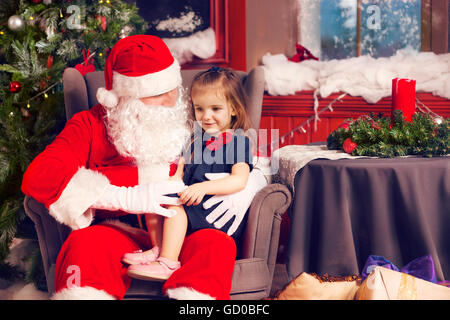 Petite fille lui disant souhaiter Noël au Père Noël près de l'arbre de Noël Banque D'Images