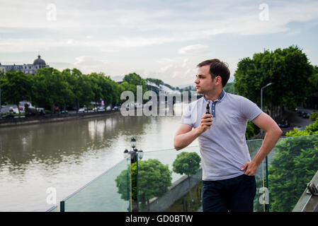 Young handsome man with e-cigarette vaping et debout sur la terrasse près de la rivière à la ville européenne Banque D'Images
