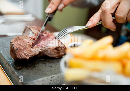 Ribeye Steak à la cuisson le goût des clients sur une pierre chaude servie avec des sauces, des frites et de la salade. Banque D'Images