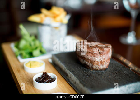 La cuisson steak goût aux clients sur une pierre chaude servie avec des sauces, des frites et de la salade. Banque D'Images