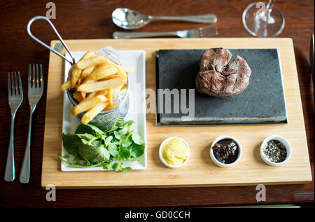 La cuisson steak goût aux clients sur une pierre chaude servie avec des sauces, des frites et de la salade. Banque D'Images