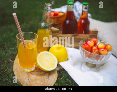 Retro un verre de limonade avec du citron sur le bureau en bois et des bouteilles de limonade avec cerise, poire et citron sur le jardin picn Banque D'Images