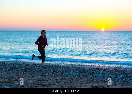 Jeune femme jogging le long de la plage de surf de mer au lever du soleil Banque D'Images