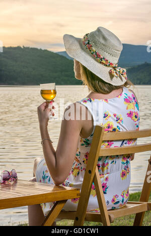 Femme avec un verre de vin au bord du lac Banque D'Images