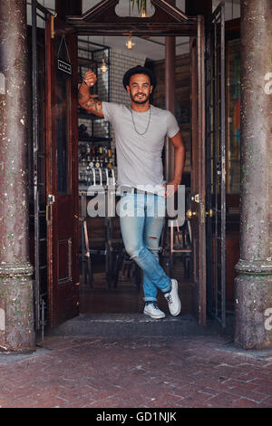 Portrait de jeune homme moderne debout à l'entrée d'un café. Jeune homme élégant au café un porte avant. Banque D'Images