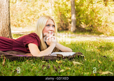 Une jeune femme aux longs cheveux blonds prévues temps personnel à l'étude de la Bible et en priant à l'extérieur dans un parc en automne ; Edmonton, Alberta, Canada Banque D'Images