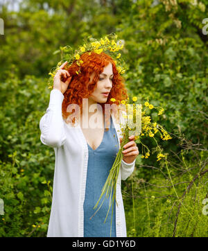 Jeune femme cheveux rouge attrayante tisse une couronne de fleurs sauvages. Fille hippie. L'unité avec la nature. Banque D'Images