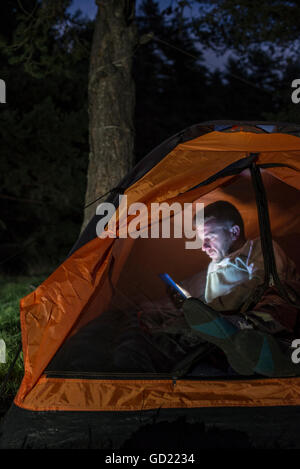 L'homme regardant son smartphone dans une tente dans la nuit. Banque D'Images