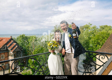 Happy wedding couple ouvrir une bouteille de champagne sur le balcon de l'immeuble Banque D'Images