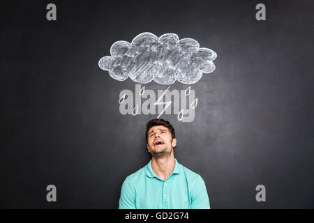 Jeune homme déprimé désespéré et permanent de pleurer sous la pluie et la foudre nuage avec tirés sur l'arrière-plan du tableau Banque D'Images