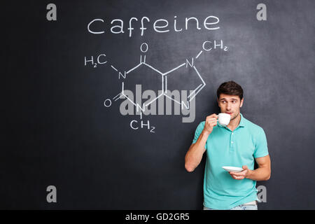 Beau jeune homme de boire du café sur tableau noir avec fond appelée structure chimique de la molécule de caféine Banque D'Images