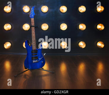 Music concept. Guitare électrique bleu debout sur le plancher en bois près du mur sous les feux de croisement Banque D'Images