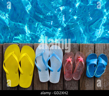 Les tongs aux couleurs vives de la famille sur fond de bois près de la piscine. Voyages d'été et vacances Banque D'Images