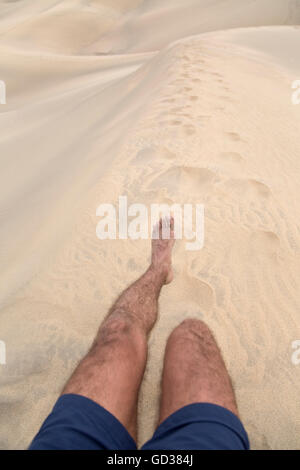 Les jambes d'un homme marchant et laissant imprimer des pieds sur le sable Banque D'Images