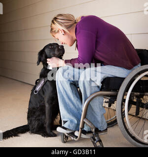 Une femme mature en fauteuil roulant caressant son chien labrador noir et le contact visuel avec le chien. Banque D'Images