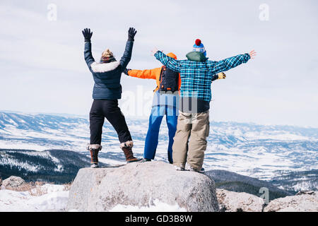 Trois personnes, deux hommes et une jeune femme debout au sommet d'une montagne avec les bras tendus. Banque D'Images