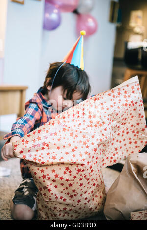 Un boy unwrapping présente à une fête d'anniversaire. Banque D'Images