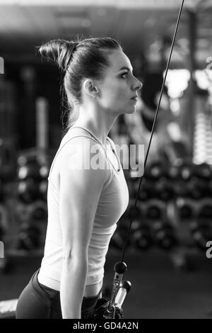 Jeune femme slim câble en pile sur la machine dans une salle de sport. Athletic Girl triceps de formation dans un centre de remise en forme. Image en noir et blanc Banque D'Images