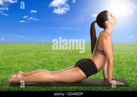 Femme qui s'étend sur le plancher sitting dans l'herbe avec un ciel bleu Banque D'Images