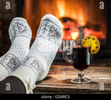 Réchauffement climatique et se reposer près de cheminée. Femme pieds près de la tasse de vin chaud devant le feu. Banque D'Images