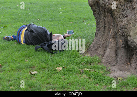 Un homme utilise son smartphone tout en flânant dans Green Park, Londres Banque D'Images