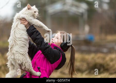 Un peu naughty girl in headphones jouant avec le chat. Banque D'Images