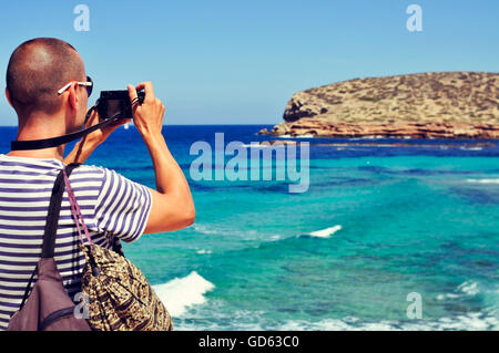 Libre d'un jeune homme de race blanche vue de derrière en prenant une photo de la mer Méditerranée et la côte de l'île d'Ibiza, Espagne Banque D'Images