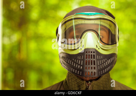 Closeup portrait man wearing jacket, vert et noir masque facial de protection debout face à l'appareil photo, l'arrière-plan des forêts, concept paintball Banque D'Images