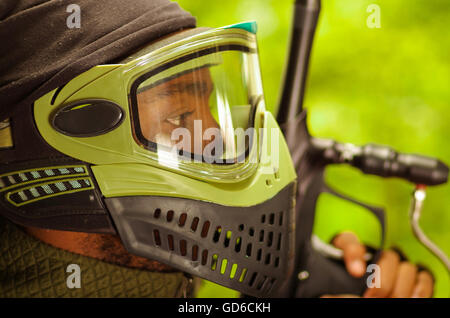 Closeup portrait man wearing green et masque facial de protection noir debout dans l'angle du profil, l'arrière-plan des forêts, concept paintball Banque D'Images