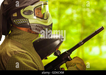 Closeup portrait man wearing jacket, vert et noir masque facial de protection de l'article profil en angle avec arme, fond de forêt, concept paintball Banque D'Images