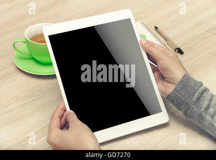 Tablet PC dans les mains, une tasse de thé et ordinateur portable sur le bureau. Banque D'Images